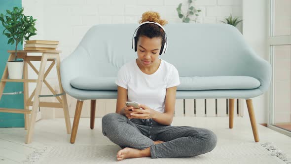 Pretty Girl Is Playing Game on Smartphone Touching Screen and Smiling While Listening To Music with