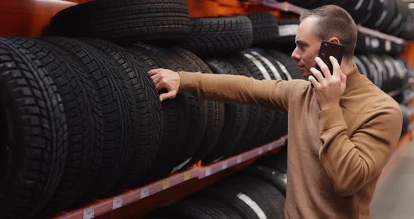 Man Chooses Winter Car Tires in Auto Shop Consulting By Smartphone