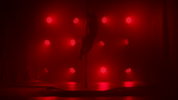 Pole Dance Practice. Dancer in Dark Studio Spin on Pole Indoors. A Silhouette Looms Against a Smoky