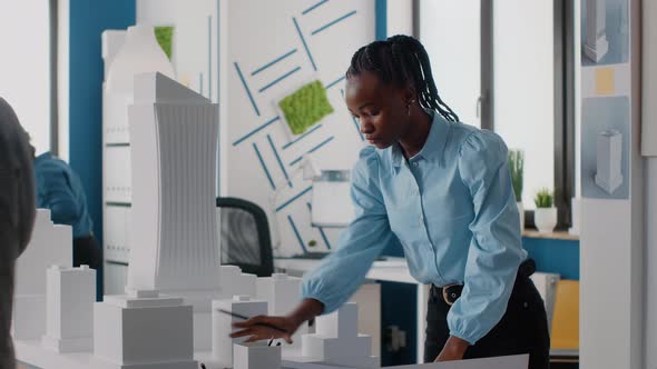 African American Woman Analyzing Blueprints Plan and Building Model to Work on Architecture