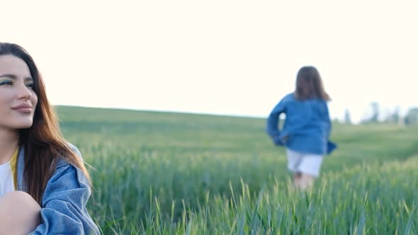 Beautiful Woman Mom and Daughter Running in the Middle of the Field on a Background of Sky