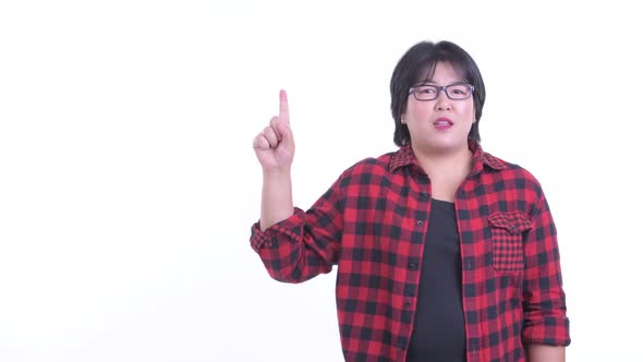Happy Overweight Asian Hipster Woman Talking While Pointing Up