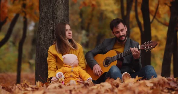 Happy Young Family with Little Baby at the Autumn Park Dad Plays on Guitar