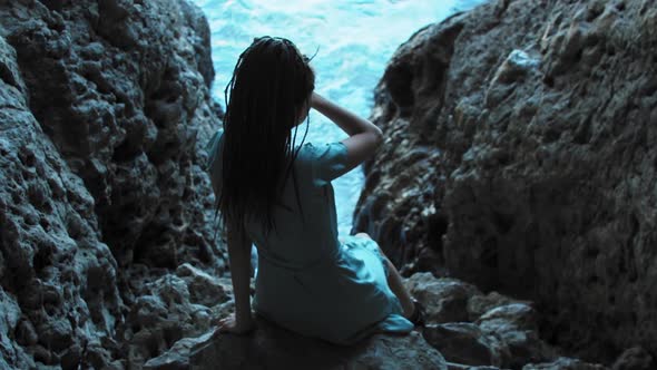 Young Woman with Dreadlocks Sitting on Rocks in Front of Sea