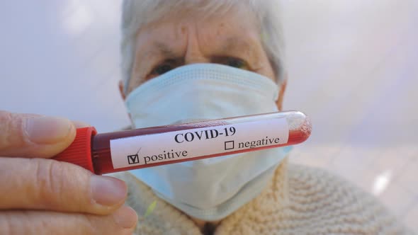 Old Lady with Protective Mask Holding Her Blood Test with Positive Result on Coronavirus. Sick