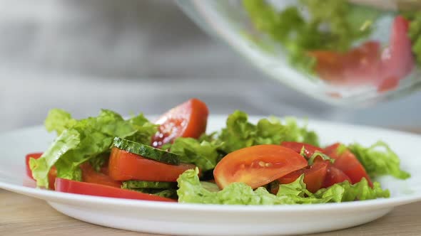 Woman putting fresh vegetable salad from bowl to plate, healthy appetizer, detox