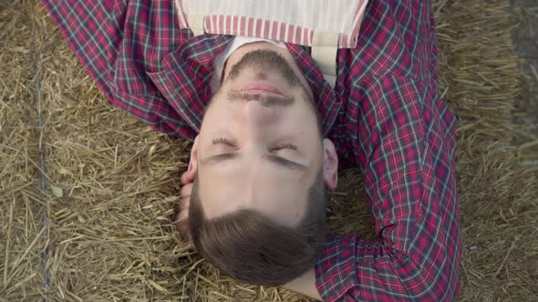 Close-up Portrait of Young Man Laying on the Hay Eating Fresh Apple