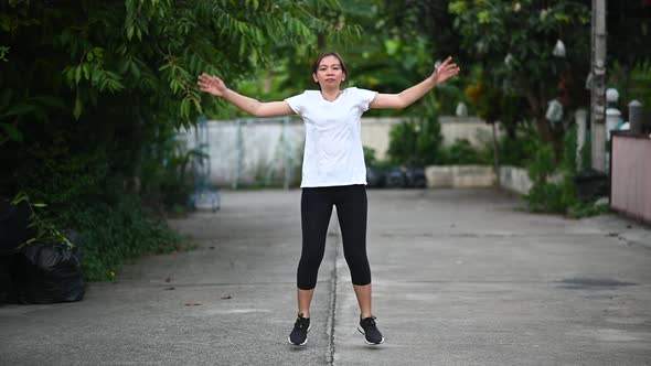 A woman wearing a white T-shirt is doing exercise by jumping and slapping.Slow motion footage.