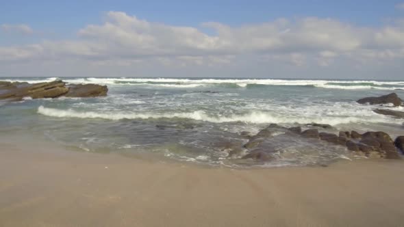 Right to left pan of waves crashing into rocks and breaking on shore.