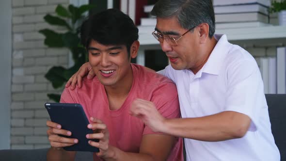 Son and senior father using digital tablet on sofa. Happy family spending time together at home.