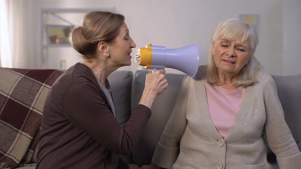 Mature Woman Speaking in Megaphone to Deaf Old Woman, Hearing Problems, Joke