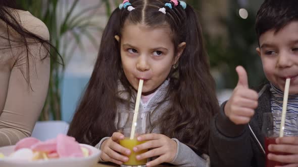 Portrait of Pretty Middle Eastern Girl Drinking Juice Showing Thumb Up with Boy and Unrecognizable