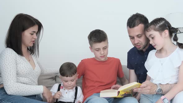 A Happy Family with Three Children Spend Time on a White Background Reading a Book Together