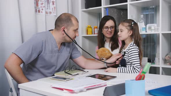 Male Doctor in the Office Takes Patients. The Family Doctor Examines a Little Girl Who's Mom Came