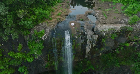 Woman in White with Arms Raised on Top of Beautiful Waterfall Looking at Sunrise