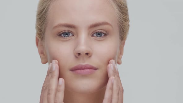 Studio portrait of young, beautiful and natural blond woman applying skin care cream. F