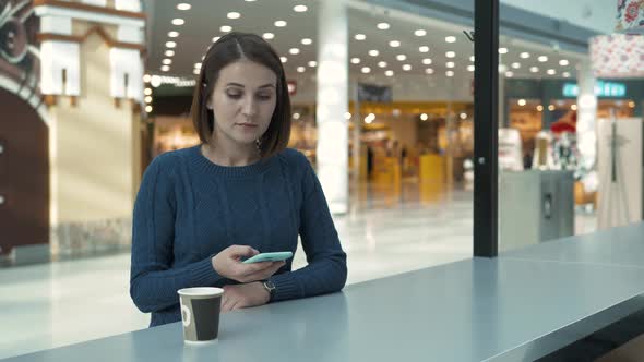 Young Woman Uses Smartphone in Free Wi Fi Zone in Shopping Mall Cafe