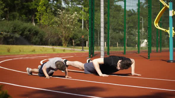 Young Father and His Little Son in Sportswear are Doing Pushups While Training at the Track of