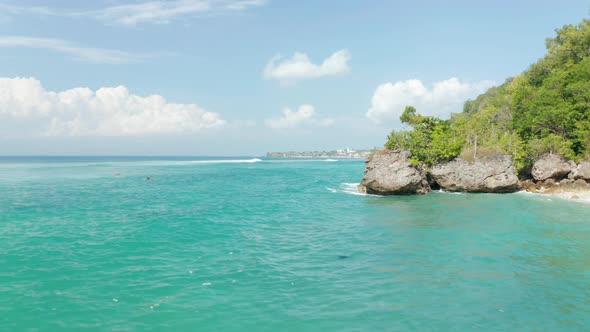 Low Aerial View of Surfers in Tropical Blue Ocean By Steep Cliffs with Luxury Villas in Bali