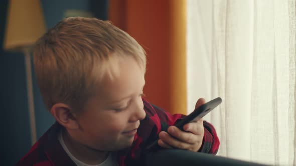 Smiling little boy is talking via video call sitting in a cozy, home-like atmosphere alt