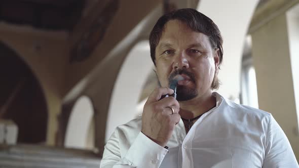 Portrait of a Brutal Young Man with a Beard That Smokes a Pipe, Then Offers It To the Viewer