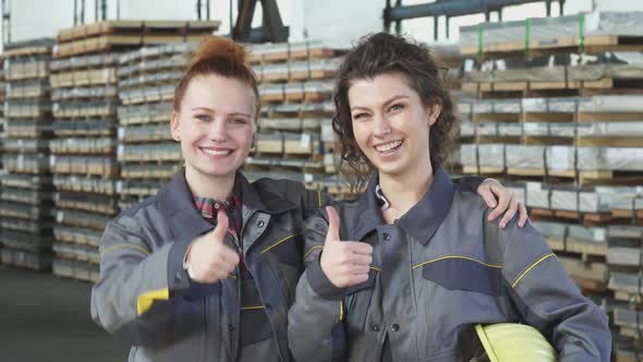Two Happy Female Factory Workers Embracing Showing Thumbs Up at the Storage