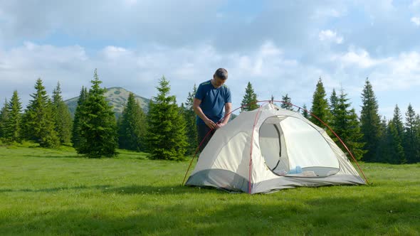 Male Tourist Puts a Tent in the Mountains