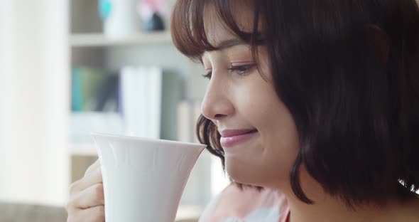 Young pretty woman drinking hot beverage while looking on TV