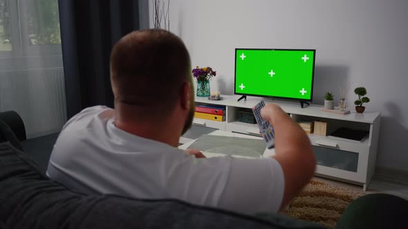 Back view Man sitting on the couch in the living room Watching TV with Green Screen