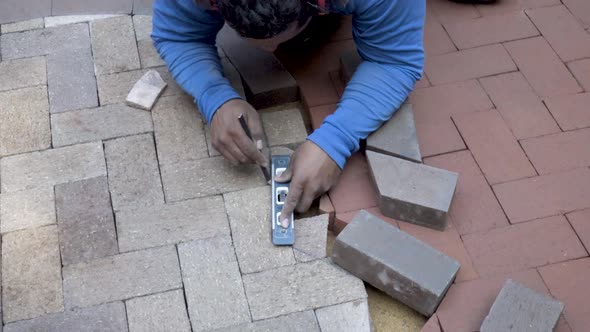 Steadicam shot of stone mason fitting and marking brick pavers for cutting for a two-tone emblem des