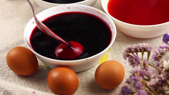 Caucasian Child Paints an Easter Egg with a Metal Spoon and Dips It Into a White Bowl with Red Dye