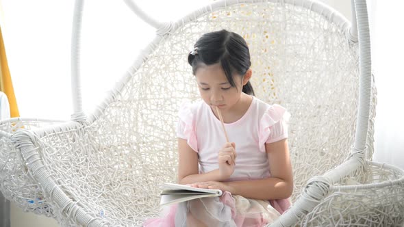 Little Asian Girl Thinking And Writing On Nest Swing