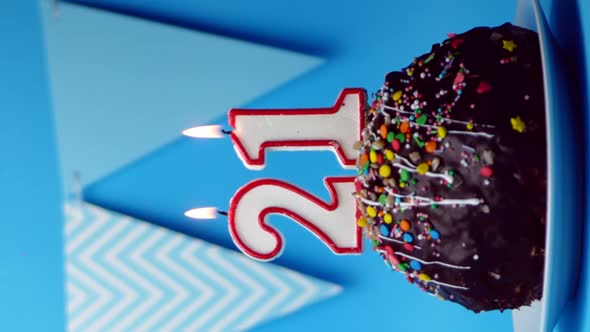 chocolate birthday cake with a burning candle number twenty one, 21 on a blue background.