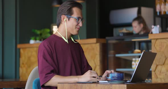 Young Handsome Man Sitting in Cafe with Laptop Making Video Calling Using Webcam and Headphones