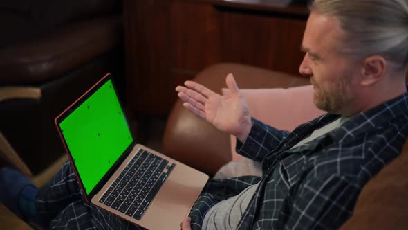 Green Screen Laptop and Man Waving Talking Sitting in Pajamas on Couch in Living Room