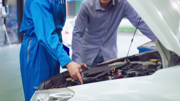 Asian automotive mechanic explain car condition to client in garage.