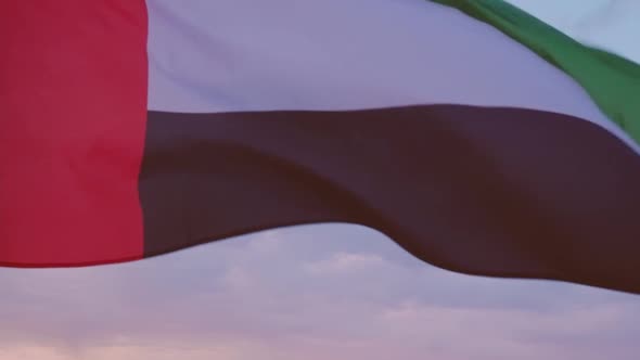 Close-up of the flag of the United Arab Emirates waving in the wind against a cloudless blue sky.