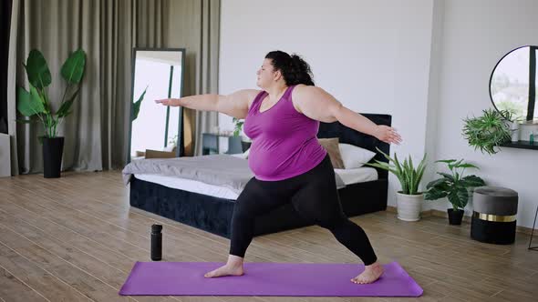 Young Overweight Woman Stands in Yoga Pose on Mat at Home