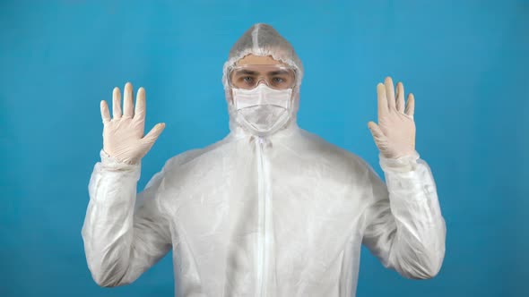 Young Man in a Protective Suit. A Man Shows Sterile Hands in Gloves on a Blue Background. Protection