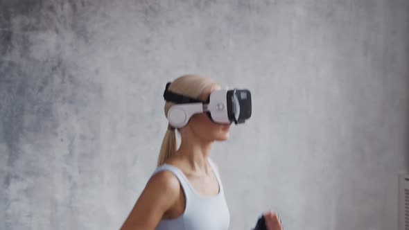 Young and sporty girl in sportswear is doing exercises at home using virtual reality helmet.