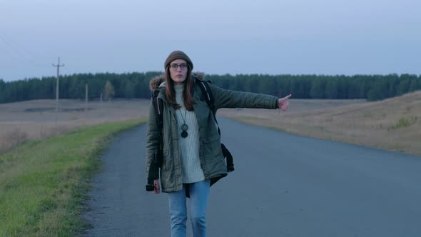 Female Tourist Can't Catch a Car in Evening Walking Along the Road.