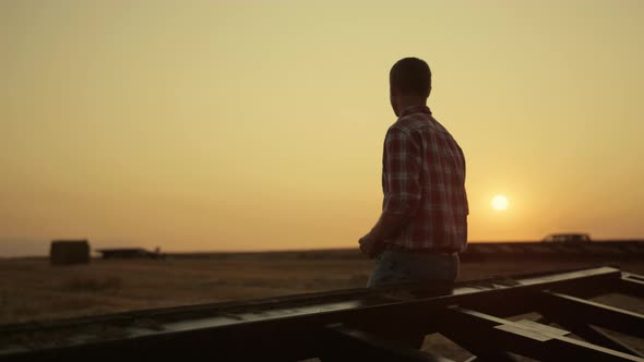 Farmer Examining Harvest on Wheat Field at Golden Sunset