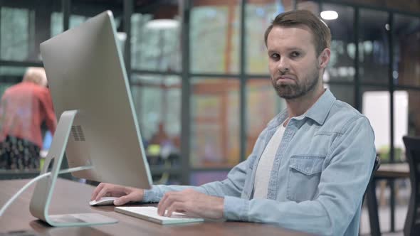 Young Man Showing Thumbs Down While Working on Computer