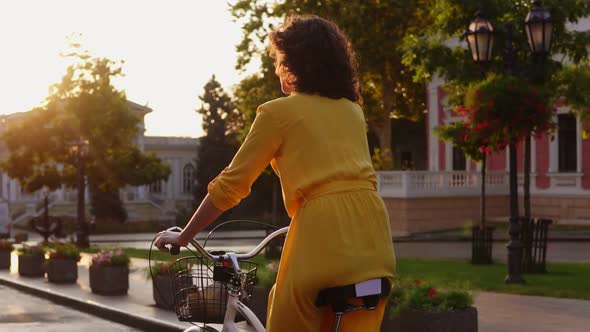 Back View of a Beautiful Woman Riding a Citybike with a Basket and Flowers in the City Center During