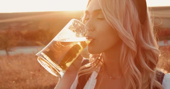 Woman with Lush Breasts Drinks Pint of Beer and Smiles Into Camera on Nature
