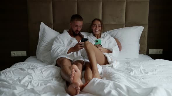 a Couple in White Coats is Lying in Bed with Phones