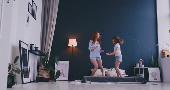 Happy Mother and Her Daughter Jumping on Bed in Children Room