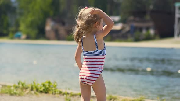 Close-up, Slow Motion: Little Girl in Bathing Suit Throws Stone at Lake, on Beach