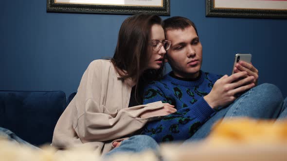 Couple Relaxes on Couch at Home, Caucasian Man Showing on Smartphone To Woman Videos, Photo, Take