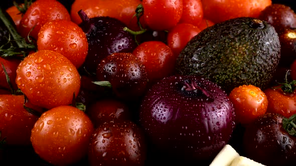 Cherry tomatoes, cucumbers, garlic, avocado and red onion on a black background in water drops